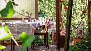Une terrasse en bois avec une table dressée pour deux personnes, entourée de plantes en pot et d’un jardin.