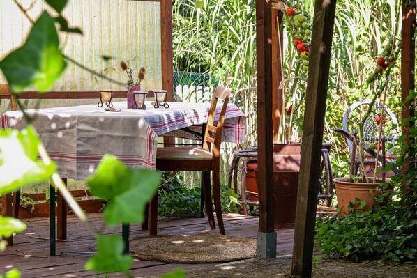 A wooden deck with a table set for two, surrounded by potted plants and a garden.