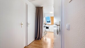 Un couloir menant à une cuisine avec une fenêtre, une porte avec un rideau et un interrupteur sur le mur.