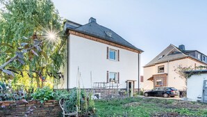 Une maison à deux étages avec un jardin, une voiture garée devant et un ciel dégagé.