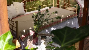 Un lit recouvert d’une couverture à rayures rouges et blanches, un vase avec des plantes vertes et un panier tressé contenant une théière.