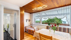 A room with a wooden ceiling, a dining table with a patterned tablecloth, a bench, and a view of greenery outside. - Apartment 'Ferienhaus Albert' with Private Terrace and Wi-Fi (Bühl)
