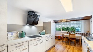 A modern kitchen with a built-in stove, a dining area with a table and chairs, and a window with a view of greenery. - Apartment 'Ferienhaus Albert' with Private Terrace and Wi-Fi (Bühl)