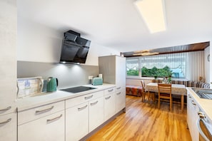 A modern kitchen with a built-in stove, a dining area with a table and chairs, and a window with a view of greenery.