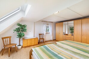 Ein Schlafzimmer mit geneigter Decke, einem Holzschrank, einem Bett mit gestreifter Bettwäsche, einer Topfpflanze, einer Holzkommode und einem Stuhl.