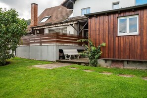 Ein Haus mit Holzwand, einem Balkon und einem Gartenbereich mit einer Bank.