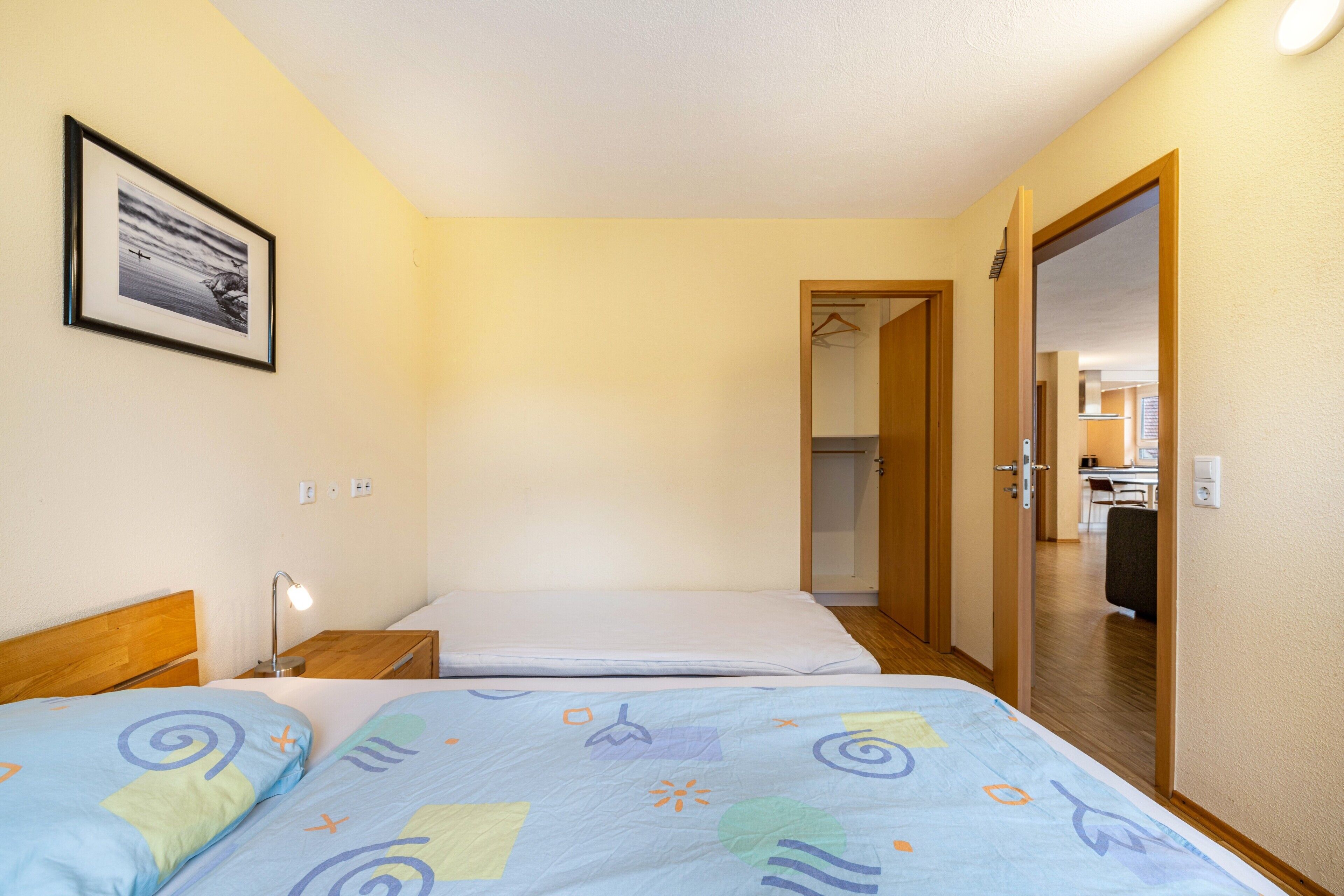 A hotel room with a bed, bedside table, and a framed picture on the wall.