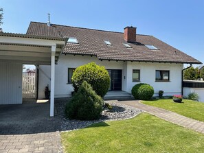 Une maison à deux étages, avec un toit en tuiles, une véranda et une pelouse bien entretenue.