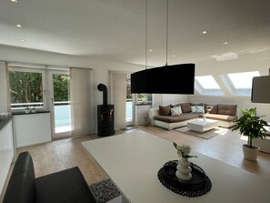 Un salon moderne avec un canapé blanc, un téléviseur noir et une table basse blanche sur laquelle est posé un vase.