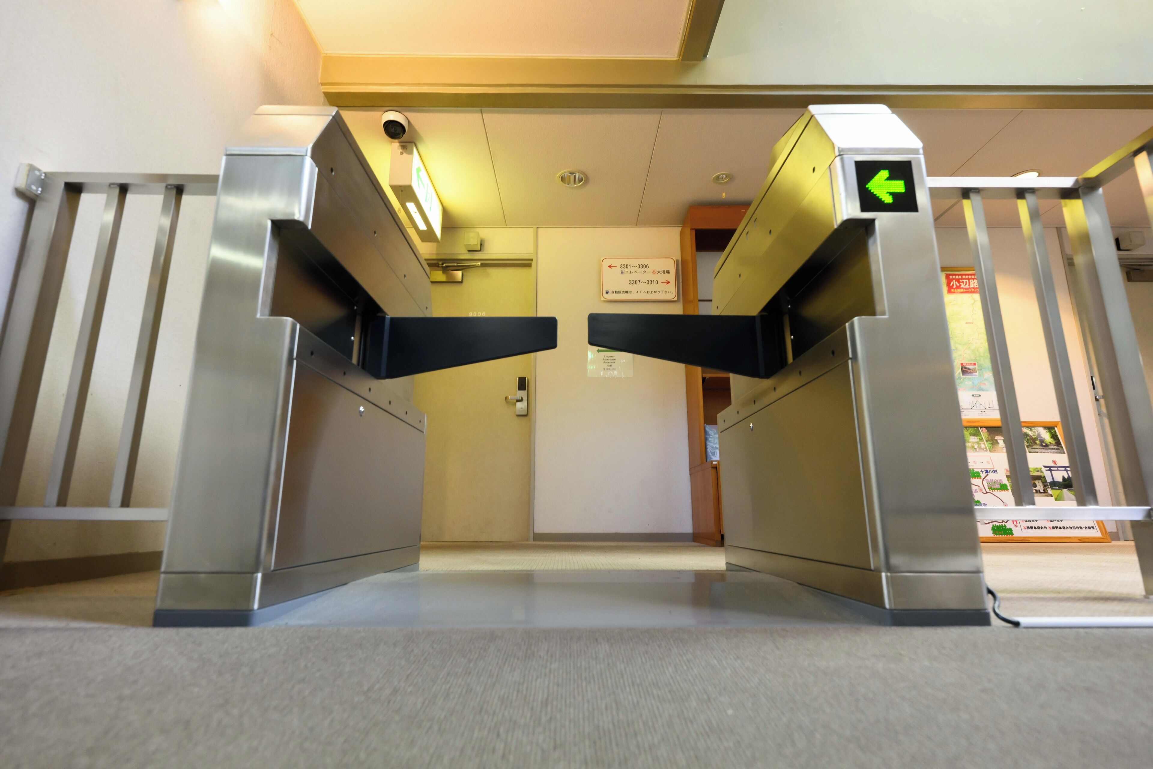 A turnstile entrance with a green directional arrow, a security camera, and a sign indicating room numbers 3301-3306 and 3307-3310.