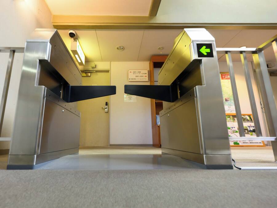 A turnstile entrance with a green directional arrow, a security camera, and a sign indicating room numbers 3301-3306 and 3307-3310.