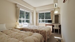 Una habitación de hotel con dos camas, un escritorio, una silla y un ventanal grande.