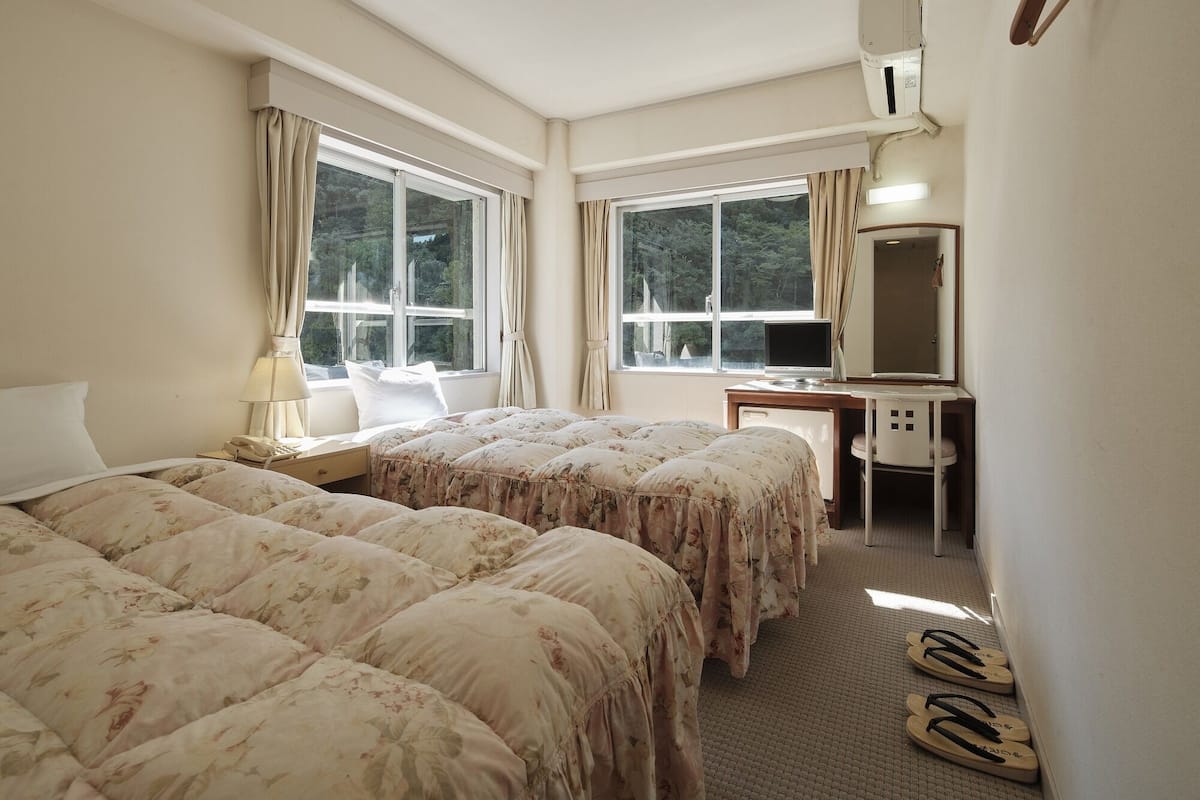 A hotel room with two beds, a desk, a chair, and a large window.