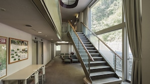 Un interior amplio con una escalera que conduce a un nivel superior, un área de descanso con sillas y un mapa en la pared.
