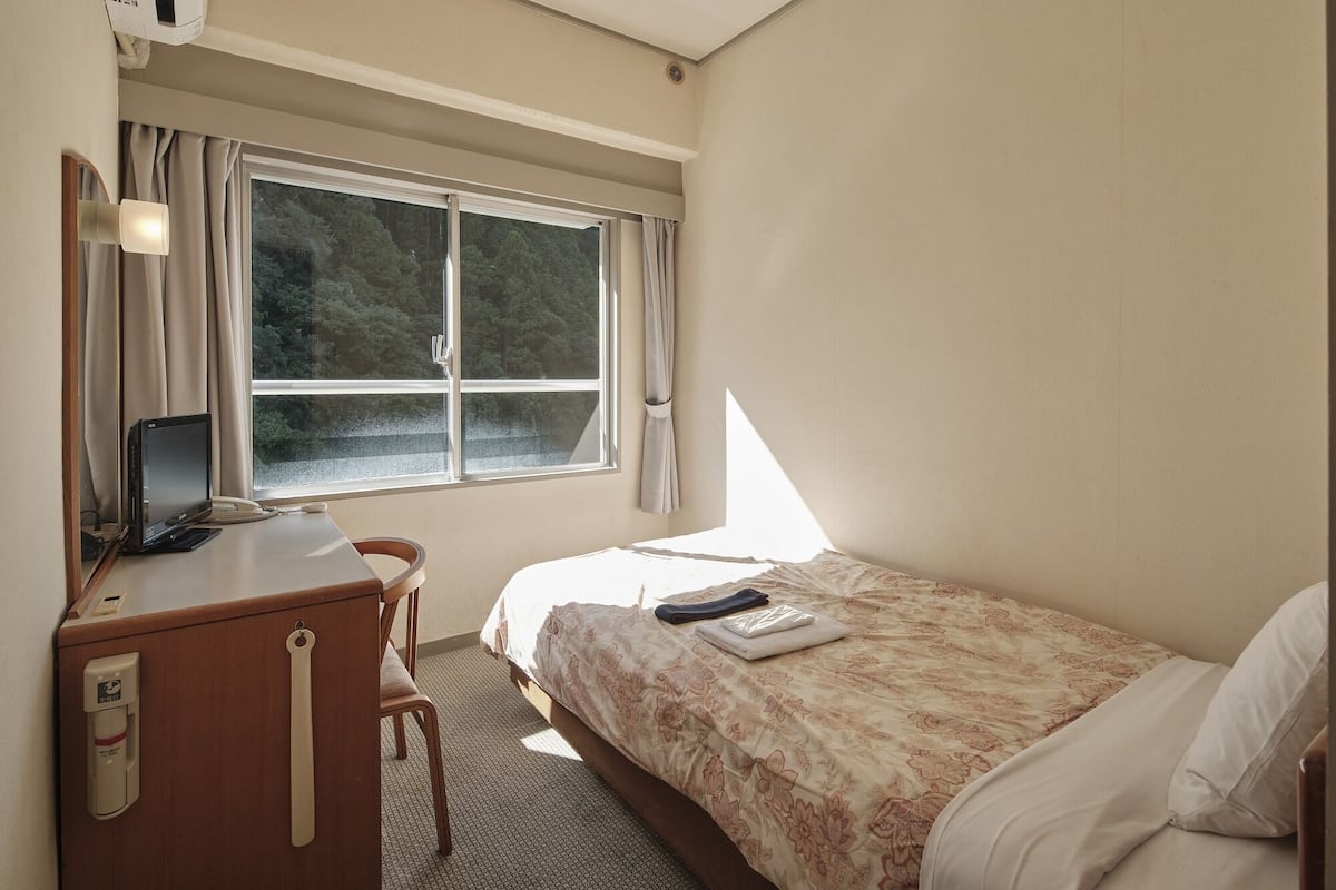 A hotel room with a bed, a desk with a computer, a chair, and a window with curtains.