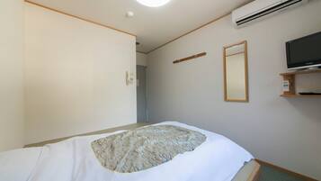 Una habitación de hotel con una cama, un aire acondicionado, un televisor y un espejo.
