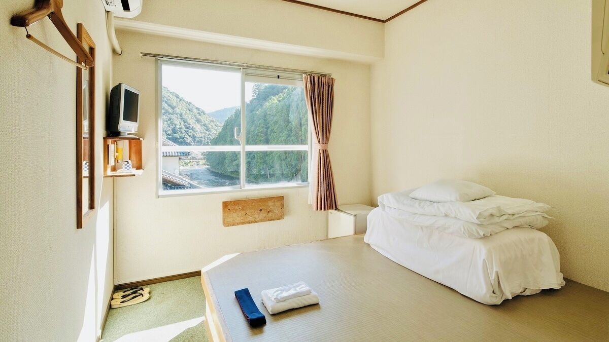 A hotel room with a bed, a TV, a window with a view of a mountain, and a small table with a remote control.