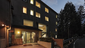 Un edificio moderno con amplias ventanas, entrada de madera y un área pavimentada con un banco de madera.