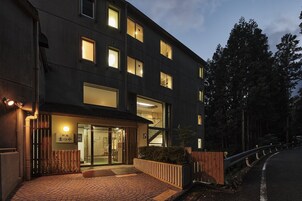 Un edificio moderno con amplias ventanas, entrada de madera y un área pavimentada con un banco de madera.