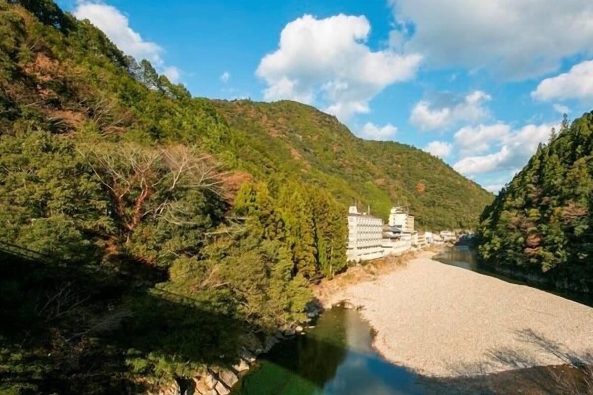 A river with a bridge, surrounded by dense green forest and hills.