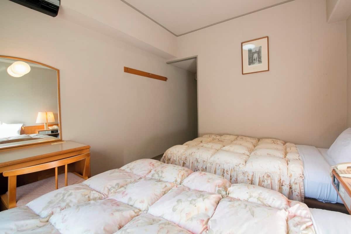 A hotel room with a bed, a desk, a chair, a bedside table with a lamp, and a framed picture on the wall.