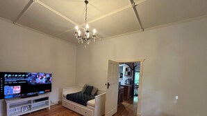 Ein Wohnzimmer mit Fernseher, einem weißen Sofa, Holzboden und einer Deckenleuchte.