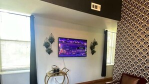 A living room with a flat-screen TV mounted on the wall, a round coffee table with a vase of flowers, and a patterned rug. - Spacious 2BR unit near BJ Hospital (St. Louis)