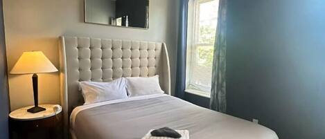 Un lit bien fait, avec une tête de lit, une lampe de chevet et un ventilateur de plafond.