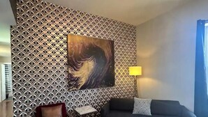 A living room with patterned wallpaper, a large abstract painting, a black sofa, a red armchair, a small table, and a round coffee table with a vase and flowers. - Spacious 2BR unit near BJ Hospital (St. Louis)