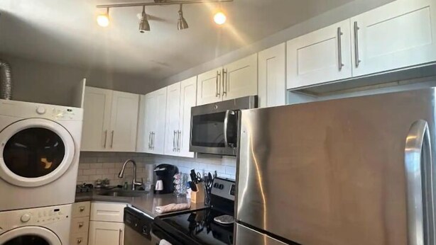 A compact kitchen with white cabinets, a stainless steel refrigerator, a microwave, a stove, and a washing machine. - Spacious 2BR unit near BJ Hospital (St. Louis)