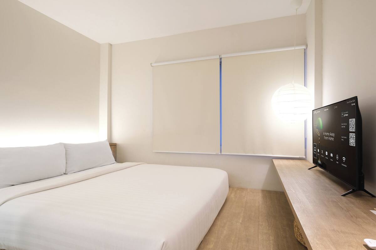 A hotel room with a bed, a desk, a TV, and a window with a blind.