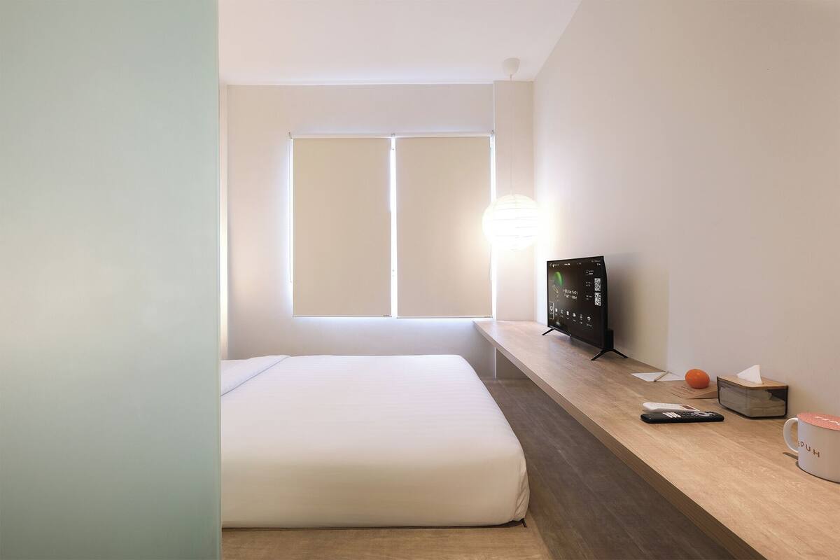 A hotel room with a bed, a desk with a computer, a lamp, and a window.
