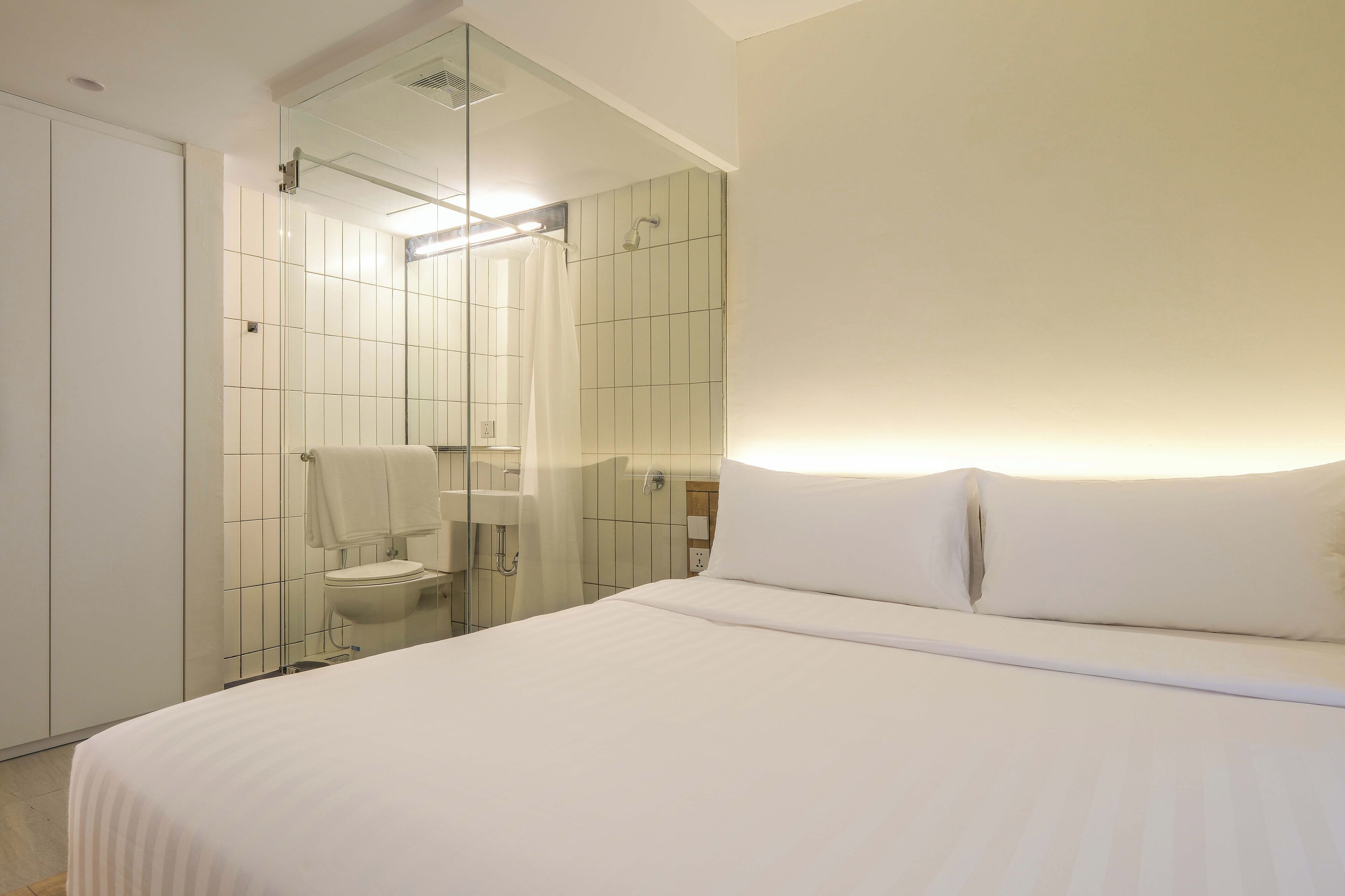 A modern hotel room with a large bed, a glass shower enclosure, and a white color scheme.