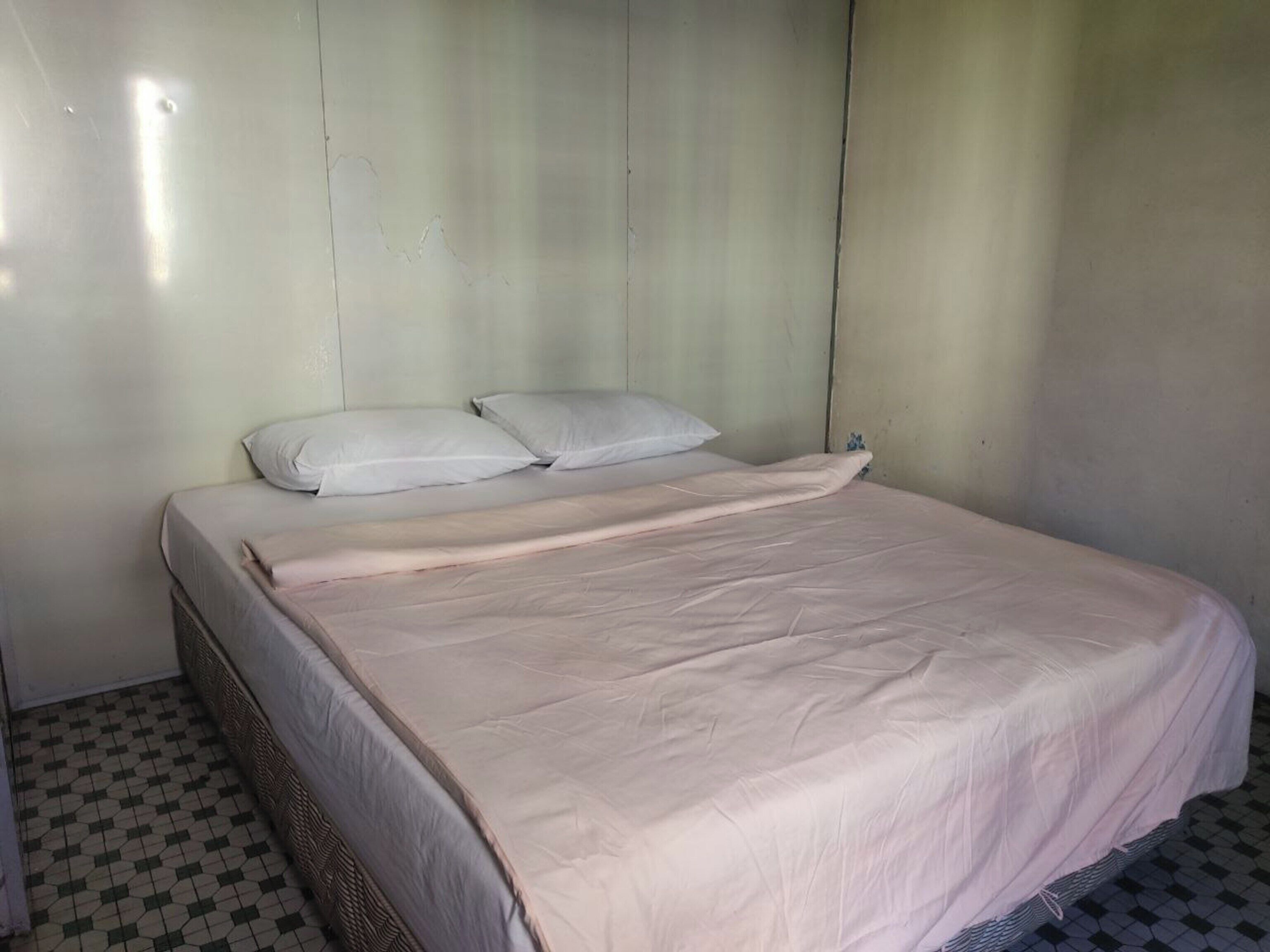Une chambre avec un lit simple, un oreiller blanc et un motif à carreaux sur le sol.