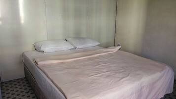 Une chambre avec un lit simple, un oreiller blanc et un motif à carreaux sur le sol.