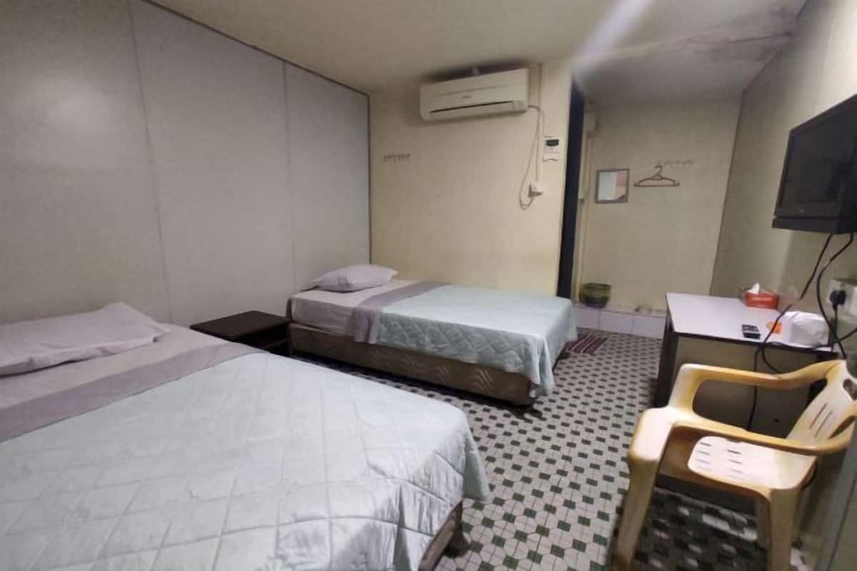 A room with two beds, a desk, a chair, an air conditioning unit, and a television.