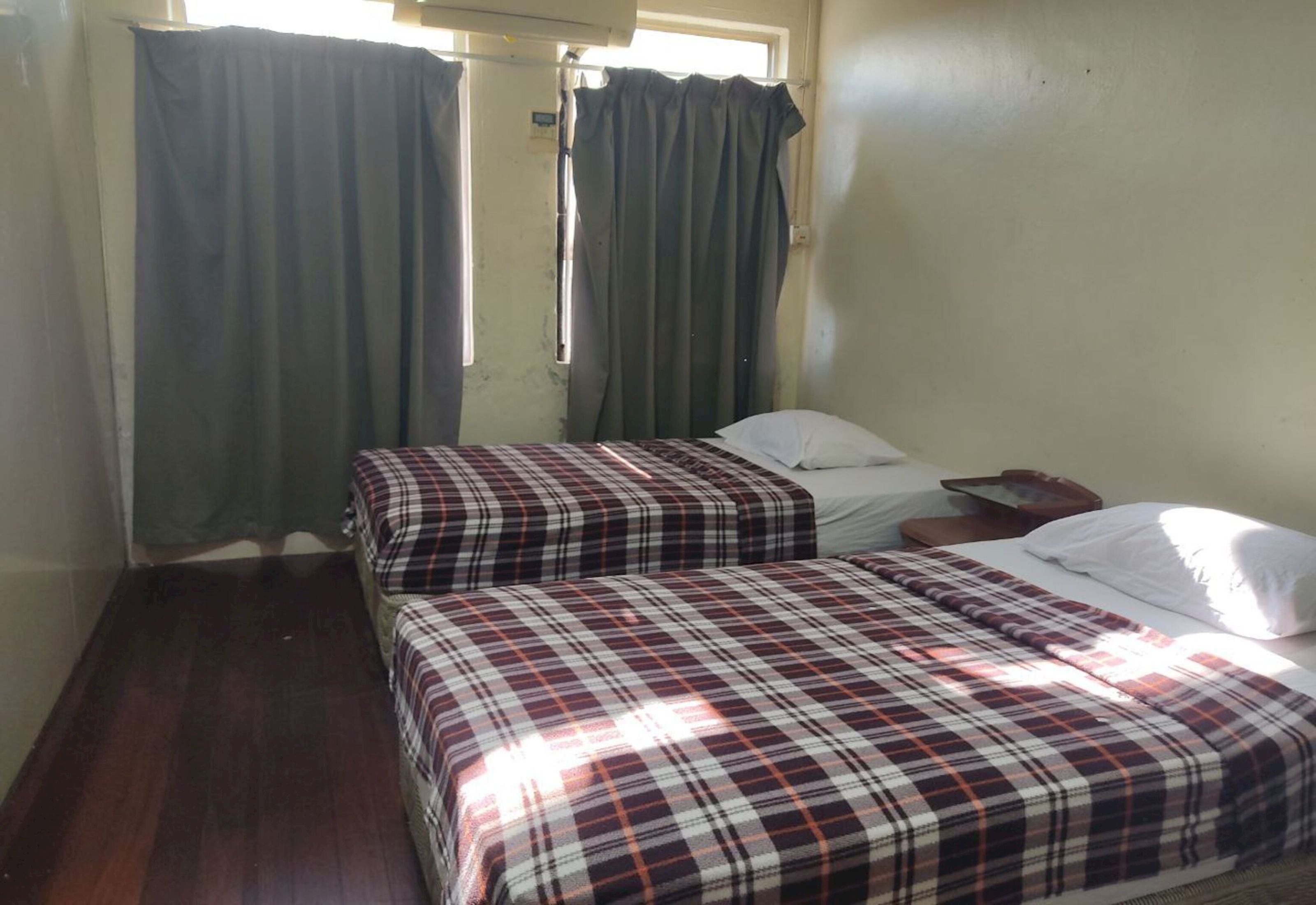 Una habitación con dos camas, cada una con una colcha escocesa, un ventanal con cortinas y suelo de madera.