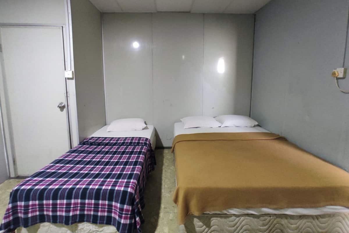 A small, single-room accommodation with two single beds, each with a different colored bedspread.
