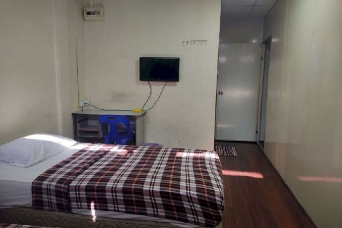 A room with a bed, a desk with a computer, a wall-mounted TV, and a door.