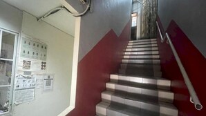 A staircase with alternating red and grey steps, a metal handrail, and a wall with various notices and a window with a metal grill. - Hotel O 59 (Sibu)