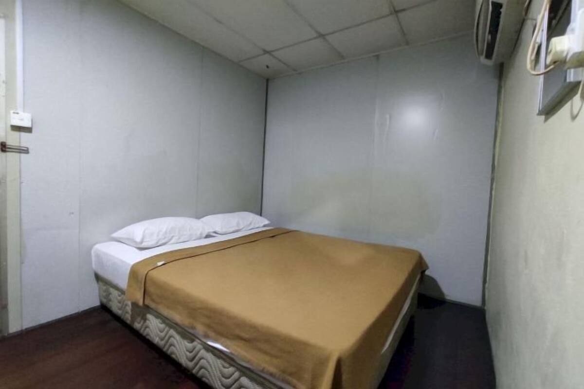 A single bed with a patterned headboard, a brown blanket, and white pillows in a room with white walls and a tiled ceiling.