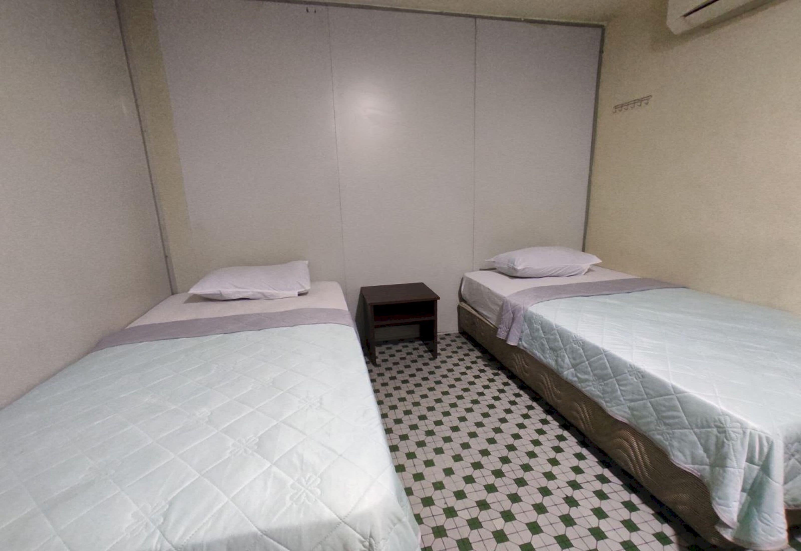 A small, clean room with two single beds, a small nightstand, and a checkered floor.