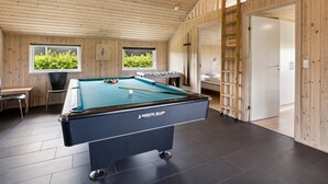 Une table de billard dans une pièce aux murs en bois et au plafond en pente.