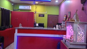 A reception area with a red counter, a ceiling fan, an air conditioning unit, and a sign indicating a 120V outlet. - Hotel Maa Bharati  (Guwahati)
