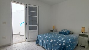 A bedroom with a bed, a nightstand, a door, and a view through the door. - La Marea Casa en Arrieta, Tranquila. Cerca de Restaurantes y Playas de Arena (CN)