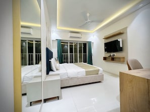 A modern hotel room with a bed, bedside tables, a desk, a TV, and a ceiling fan.