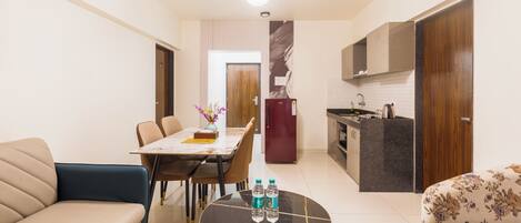 Una sala de estar moderna con un sofá, una mesa de centro con botellas de agua, un comedor con sillas y una cocina con refrigerador y armarios.