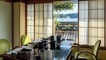 Una habitación japonesa tradicional con suelo de tatami, una mesa baja con utensilios para la ceremonia del té, y vista a un cuerpo de agua a través de paneles shoji.