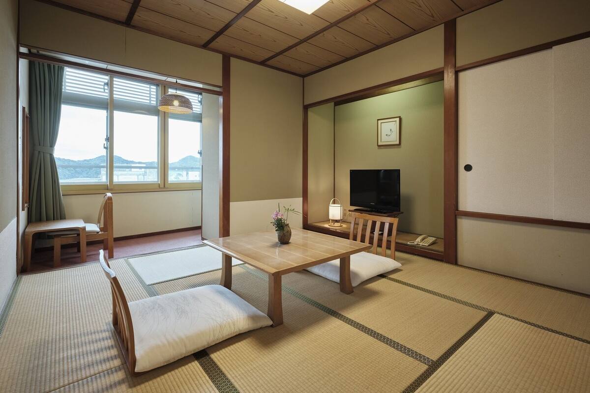 A traditional Japanese room with tatami flooring, a low table, a television, and a view of the outdoors.