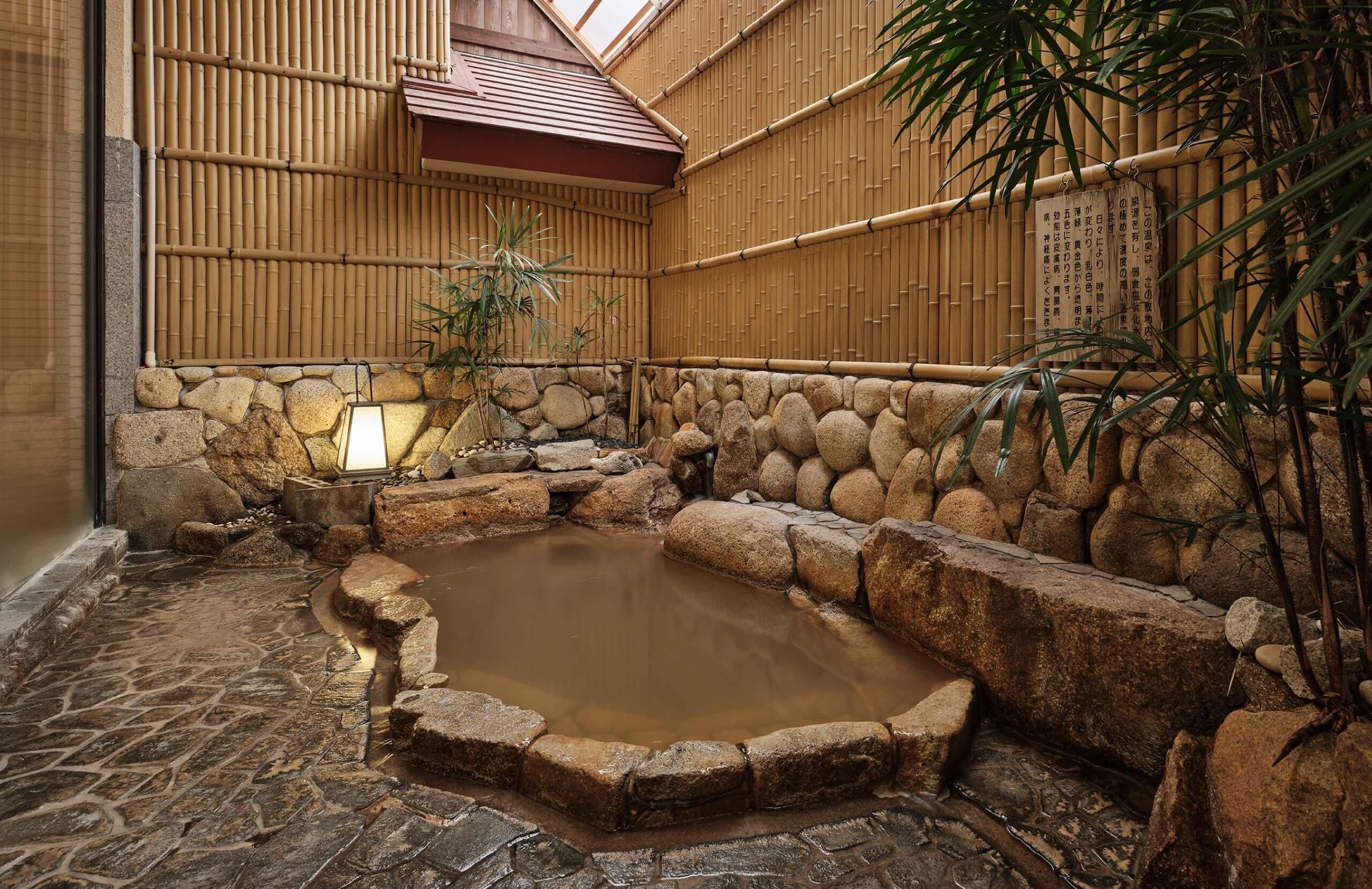 Un onsen japonais traditionnel, avec un bain en pierre entouré de rochers et de murs en bambou.
